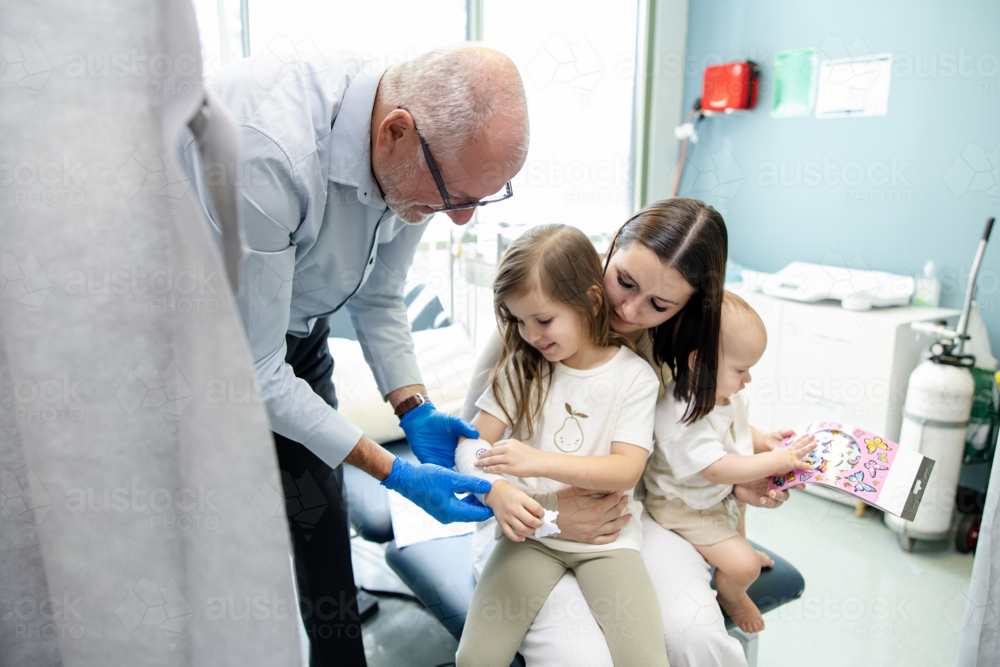 Doctor wrapping young girls arm with white bandage - Australian Stock Image