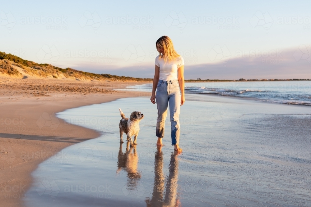 Dog and woman walking on the beach at sunset - Australian Stock Image