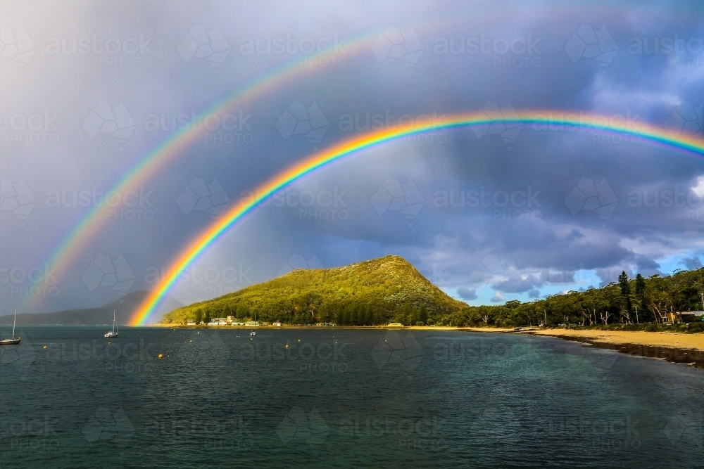 Double rainbow over mountain and ocean against cloudy sky - Australian Stock Image