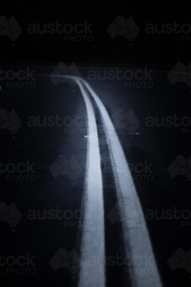 Double unbroken white road lines surrounded by darkness - Australian Stock Image