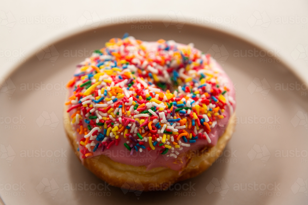 doughnut with pink icing and rainbow sprinkles - Australian Stock Image