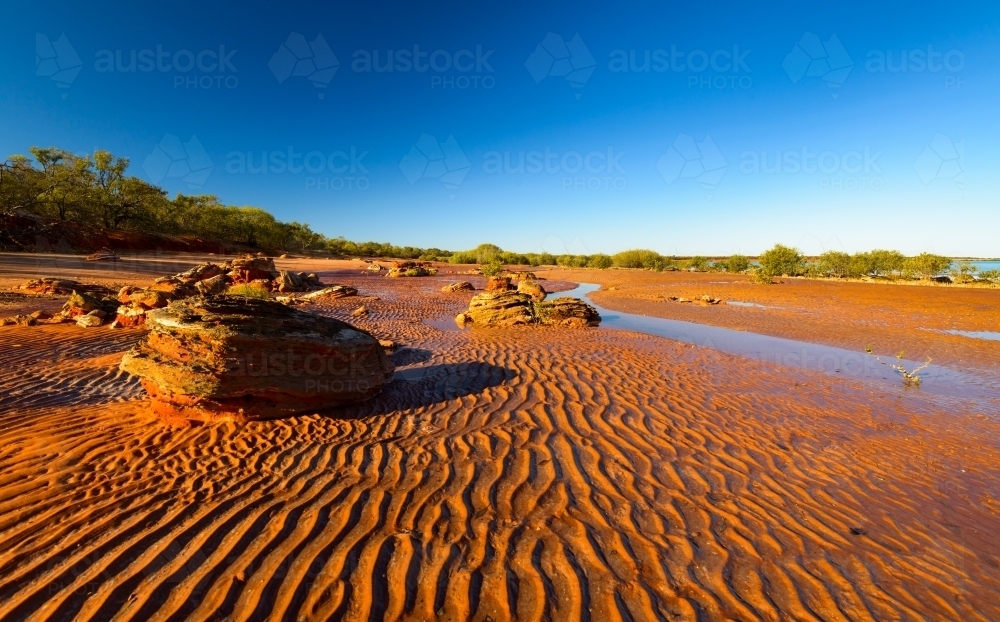 Dramatic lines of rippled orange sand with colourful rocks and clear blue sky - Australian Stock Image