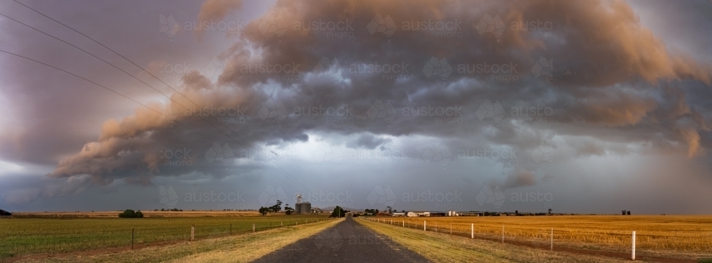 Dramatic storm clouds over a country road and flat farmland - Australian Stock Image