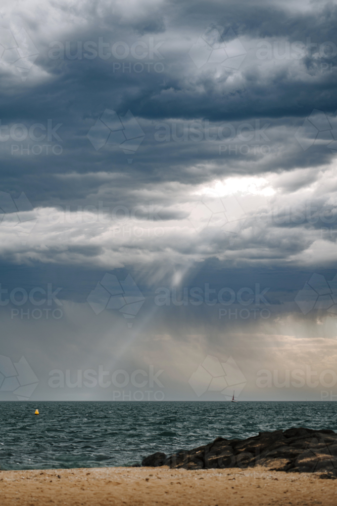 Dramatic storm clouds with sunlight illuminating ocean horizon - Australian Stock Image