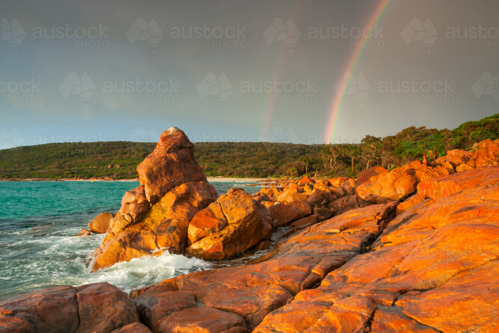 Dramatic storm lighting and a double rainbow over colourful coastal rock formations - Australian Stock Image