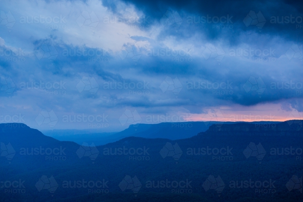 Dramatic stormy sky over layered blue mountains at nightfall - Australian Stock Image
