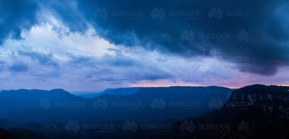 Dramatic stormy sky over layered blue mountains at nightfall - Australian Stock Image