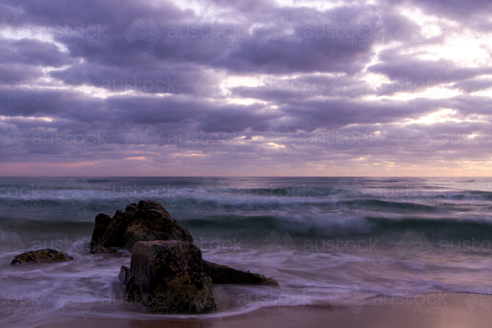 Image of Dramatic sunrise over the ocean and boulders on beach at dawn ...