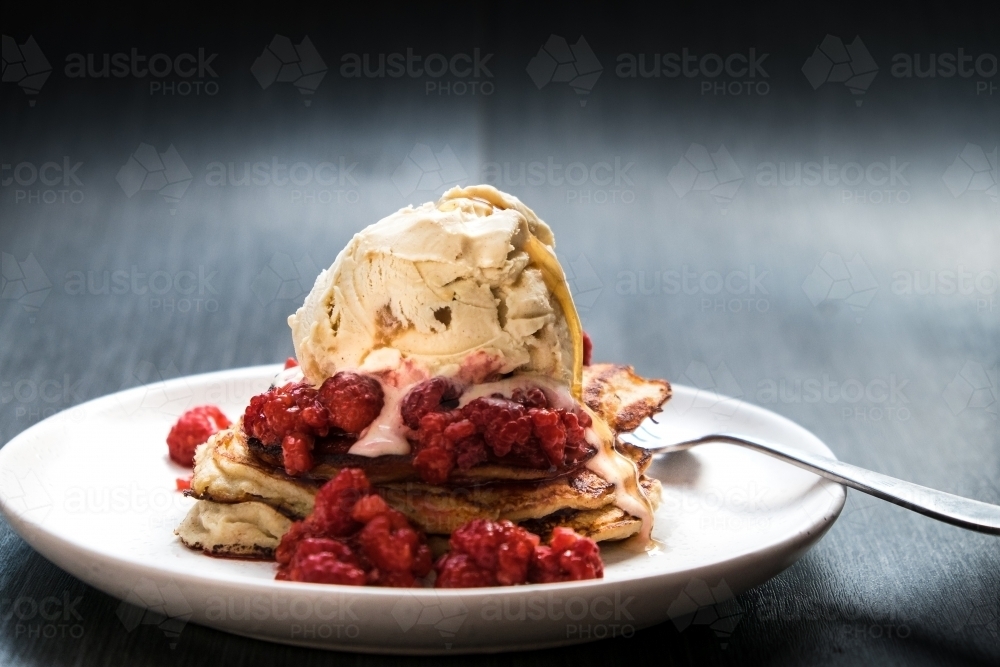 Drip of syrup slides down a scoop of ice cream on a pancake stack - Australian Stock Image