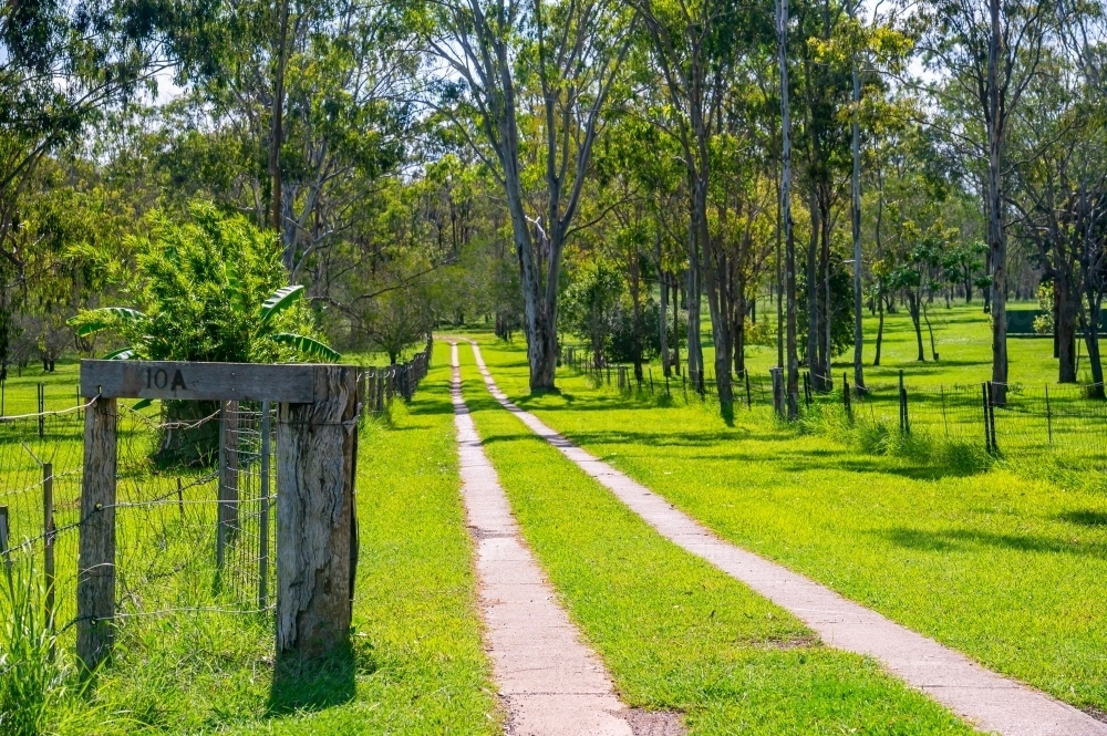 Driveway to house with vibrant green grass and wooden fence and house number - Australian Stock Image