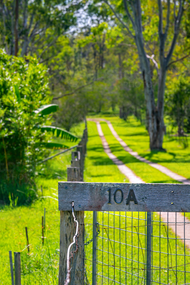 Driveway to house with vibrant green grass and wooden fence with house number in countryside - Australian Stock Image