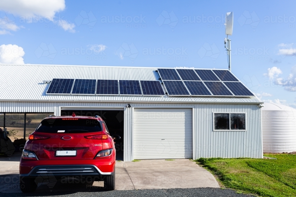 Driving electric vehicle car into solar and wind powered shed on country farm  - living sustainably - Australian Stock Image