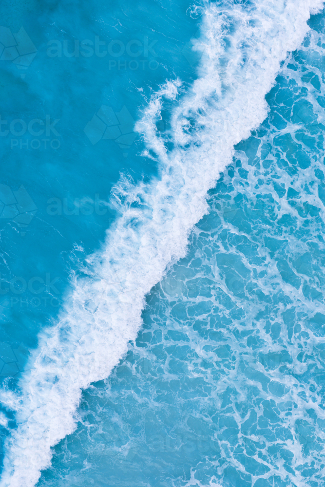 Drone overhead of white foamy waves rolling onto beach - Australian Stock Image