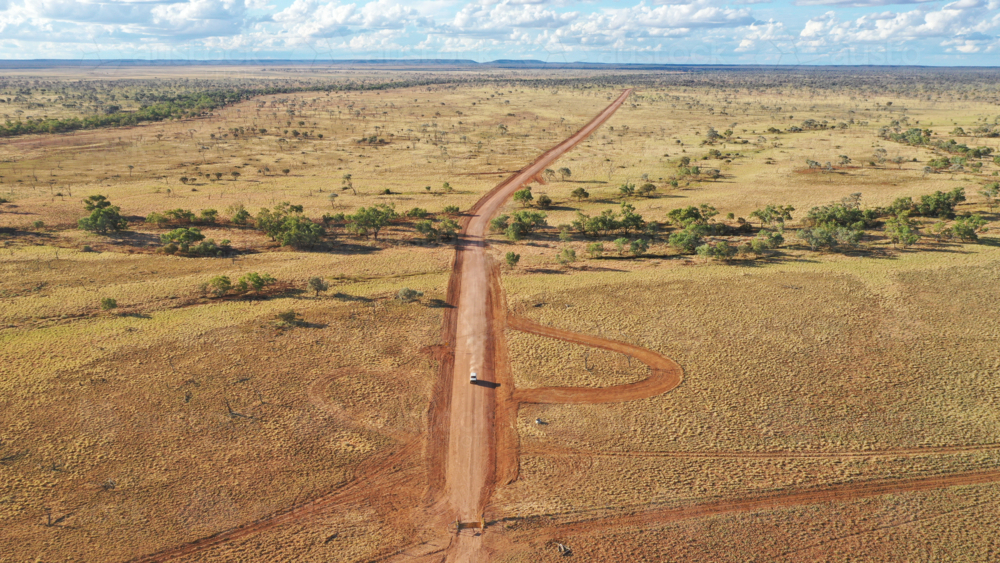 Drone shot of a vehicle driving down a dirt road - Australian Stock Image