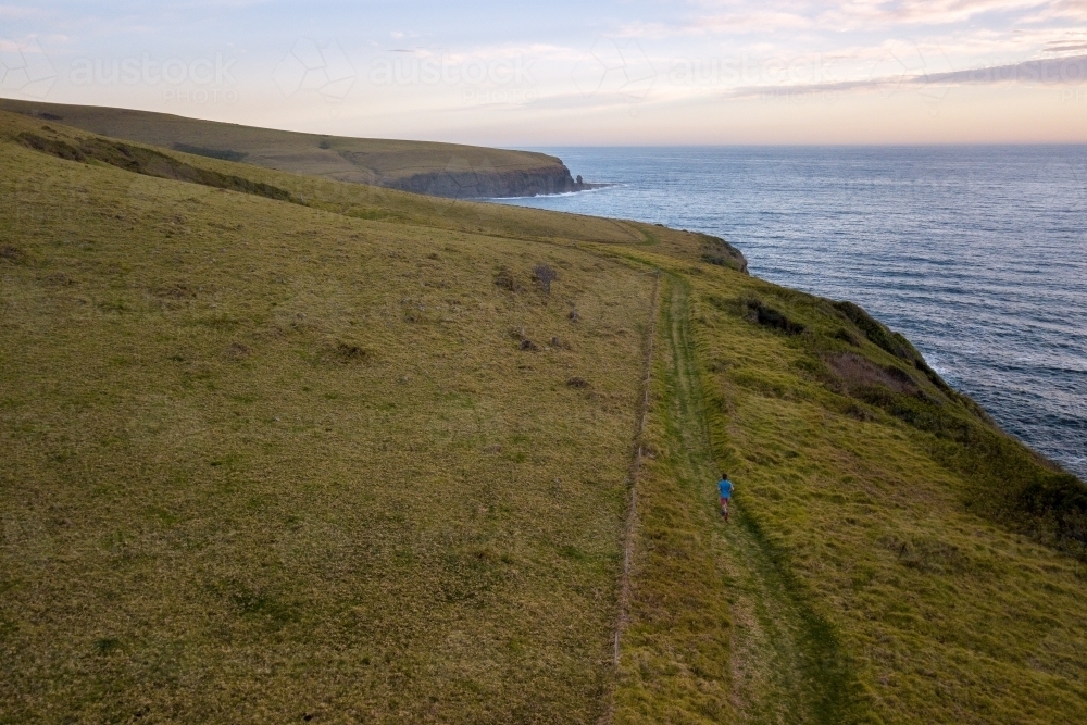 Drone Shot of Man Running on Headland Overlooking Ocean - Australian Stock Image