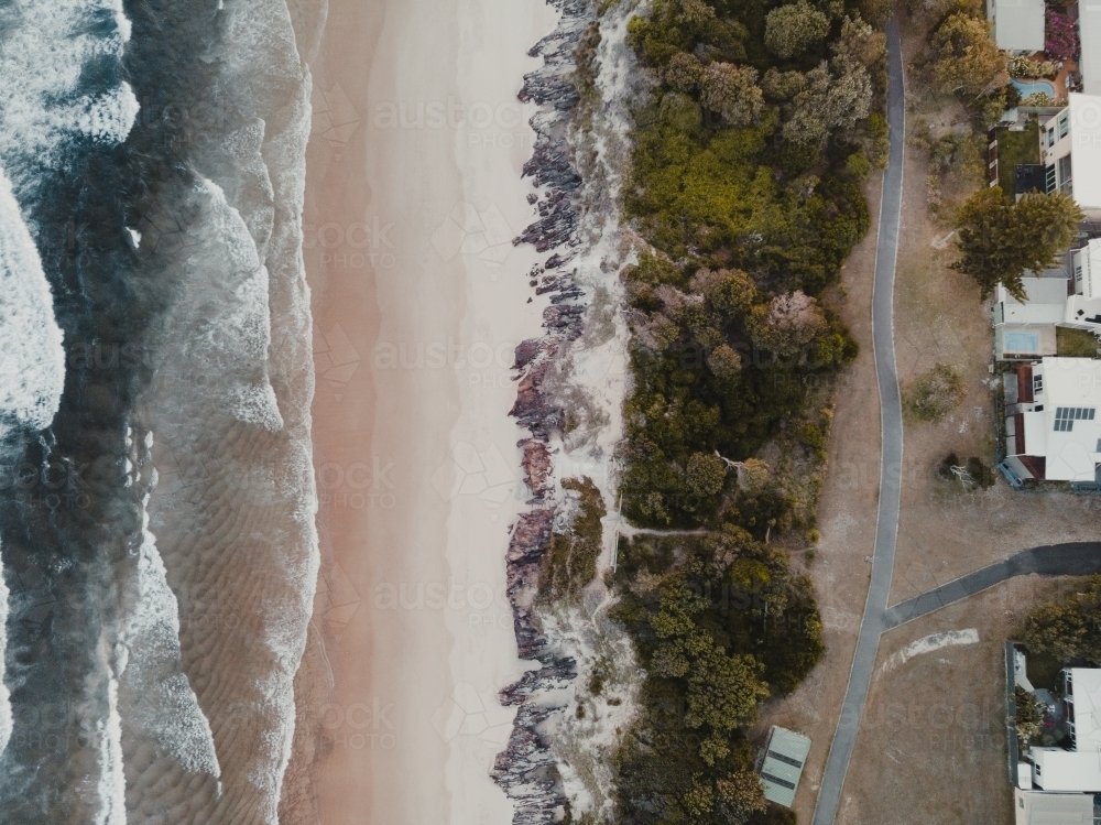 Drone shot of waves crashing on a beach with beachfront properties - Australian Stock Image