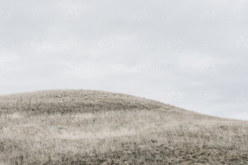 Dry, grassy hill with grey sky - Australian Stock Image