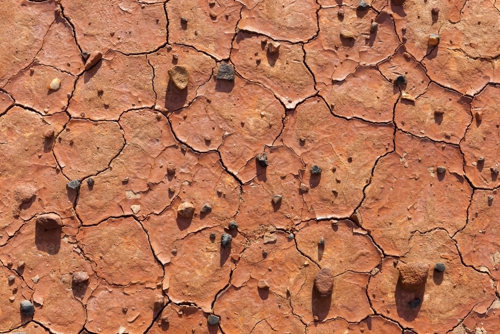 Dry red cracked earth with little pebbles lying atop - Australian Stock Image