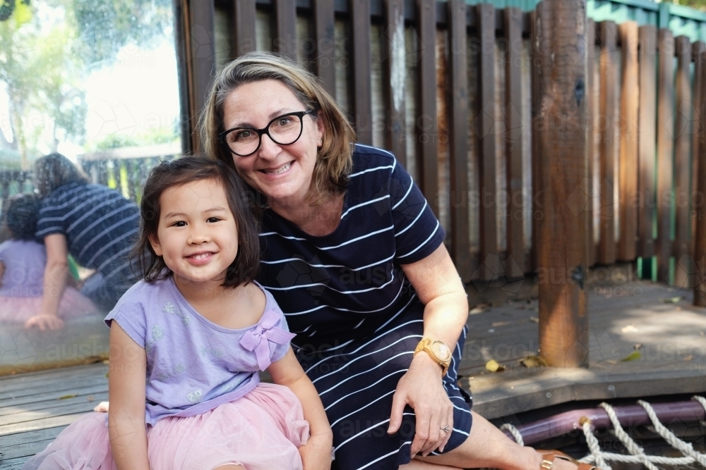 Happy multicultural teacher and child in kindergarten playground - Australian Stock Image