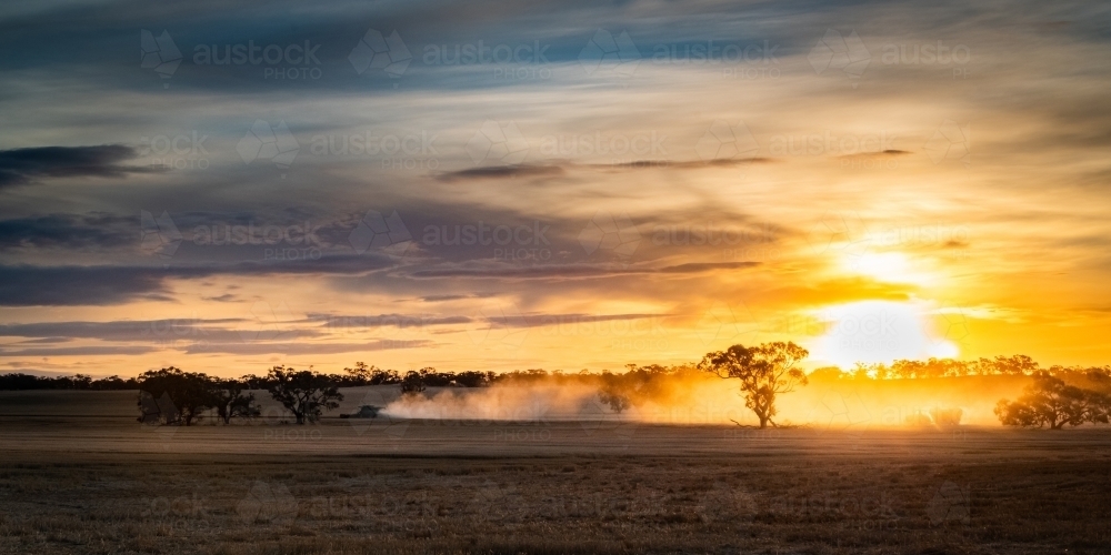 Dust from harvester flies into the air as the sun sets over the vast farming land - Australian Stock Image