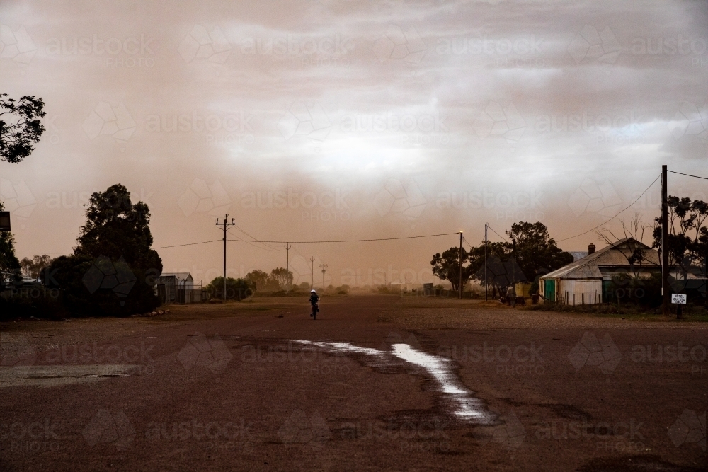 Dust storm hitting small remote town with a child riding a bike on the road - Australian Stock Image