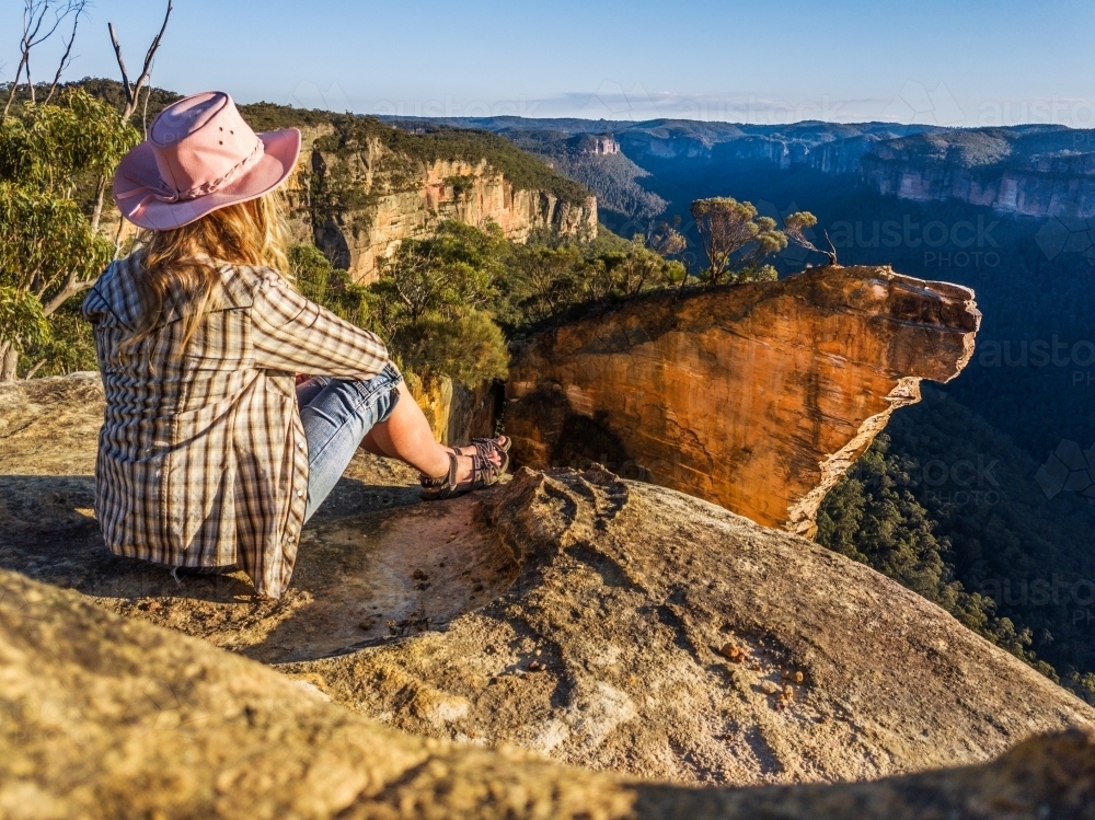Early morning chilling out on the cliff top ledge gazing over to Hanging Rock, the morning sunlight  - Australian Stock Image
