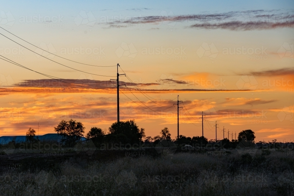 Early morning dawn colours of the sky with the power line silhouettes lead into the distance - Australian Stock Image