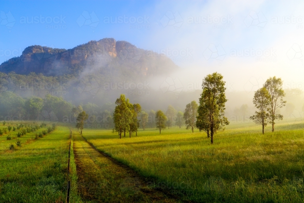 Early morning fog clearing over a rural scene and mountain - Australian Stock Image