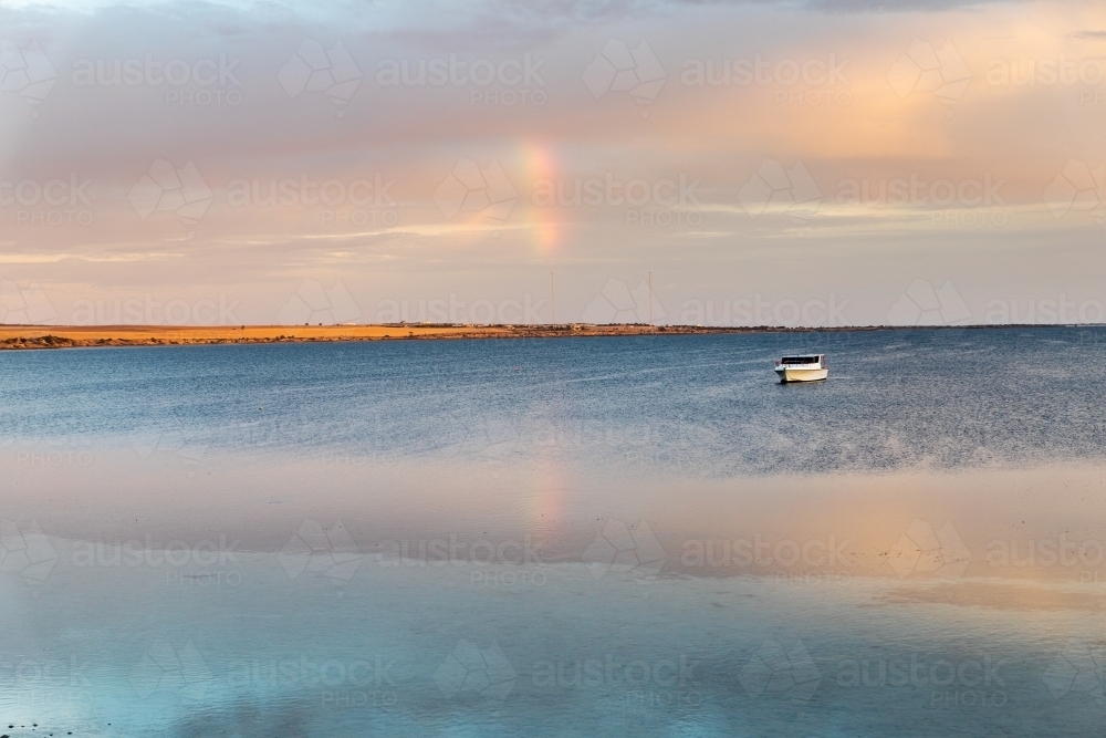 early morning light over calm bay with moored boat - Australian Stock Image
