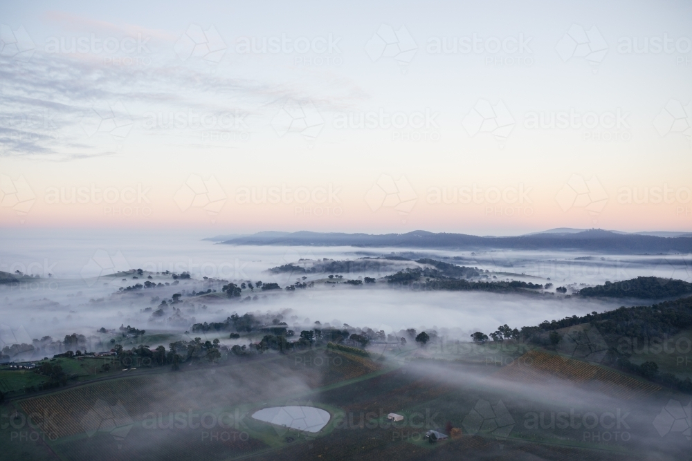 Early morning mist and low-lying clouds settled in the valleys between rolling-hills. - Australian Stock Image