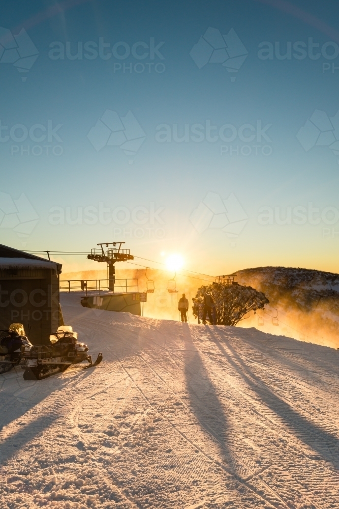 earlybird skiers heading down the slopes, silhouetted against the rising sun - Australian Stock Image