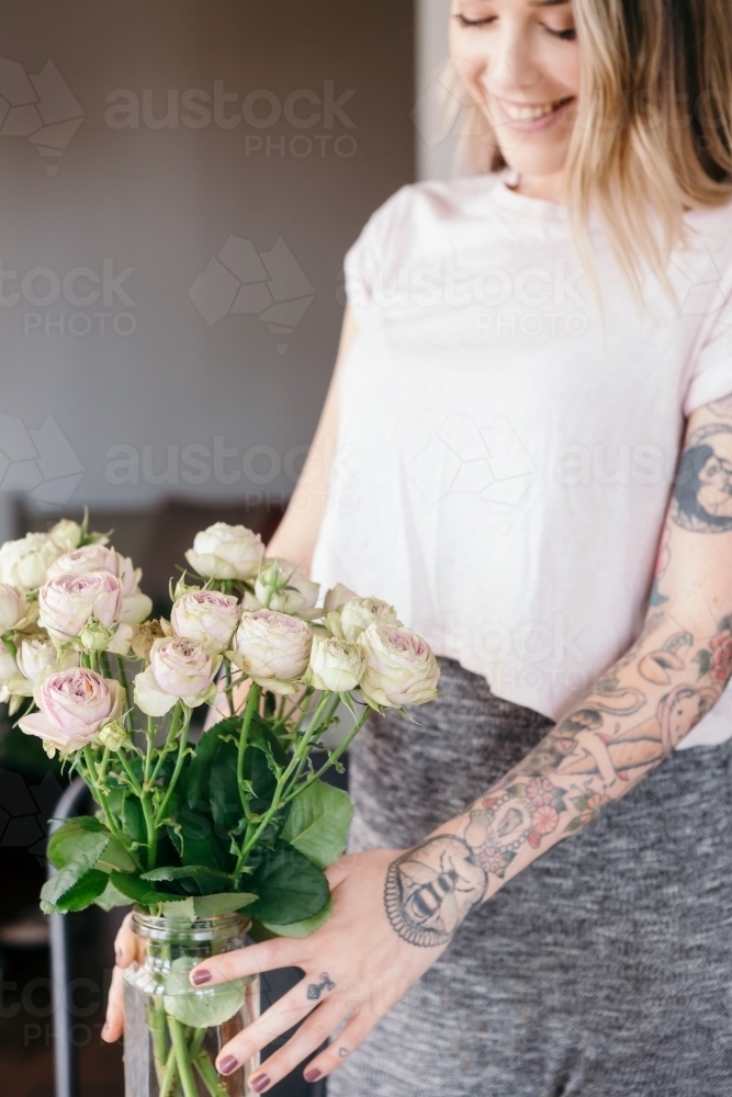 Edgy girl with sleeve tattoos arranging a pretty vase of roses - Australian Stock Image