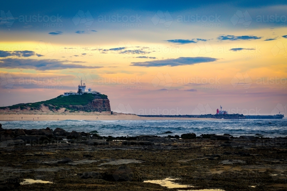 Eerie sunset at Nobby's Beach in Newcastle with cargo ship passing the headland - Australian Stock Image