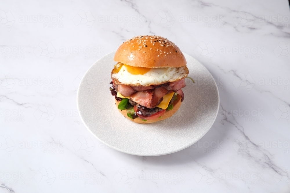 Egg and bacon burger on plate on marble table - Australian Stock Image