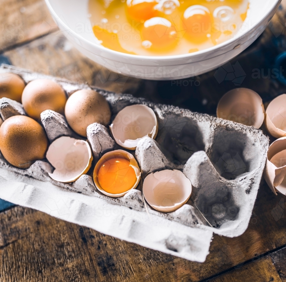 Egg cardboard with egg yolk and cracked eggs inside in a wooden background - Australian Stock Image