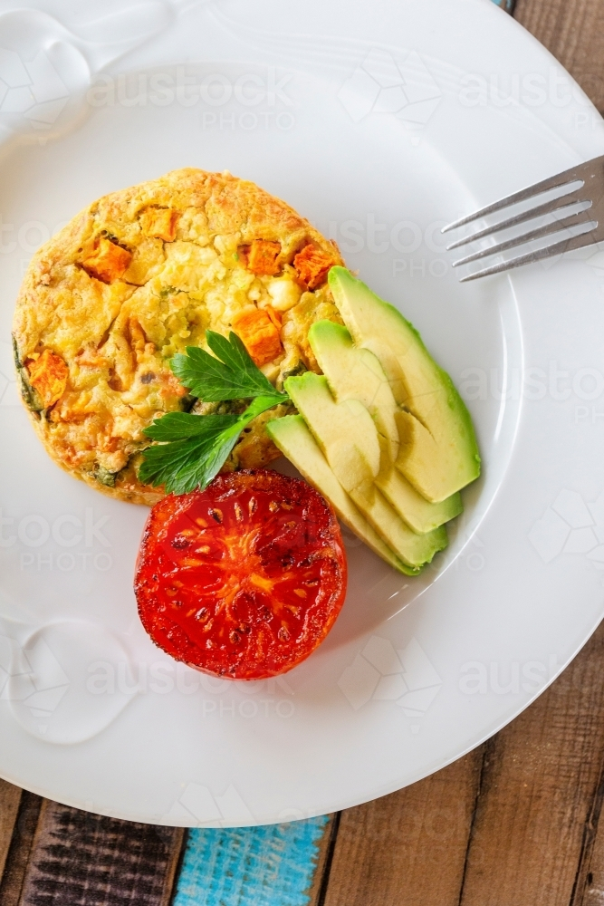 Egg omelet with avocado slices and grilled tomato on a plate. - Australian Stock Image