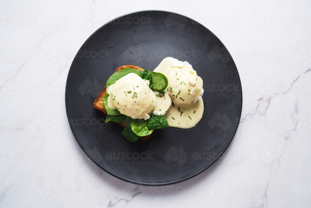 Eggs Florentine drizzled with creamy Hollandaise sauce and served on a black plate. - Australian Stock Image