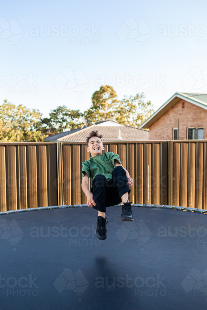 Eight year old Aussie kid jumping and doing flips on trampoline in backyard of suburban home - Australian Stock Image