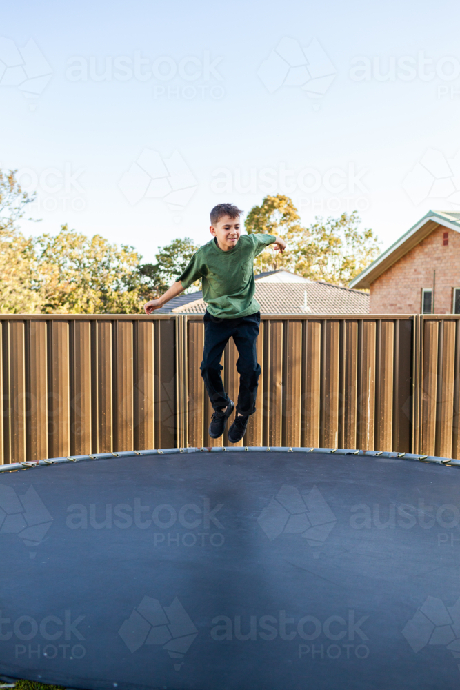 Eight year old Aussie kid jumping and doing flips on trampoline in backyard of suburban home - Australian Stock Image