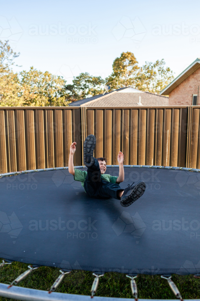 Eight year old Aussie kid jumping and doing flips on trampoline in backyard of suburban home - Australian Stock Image