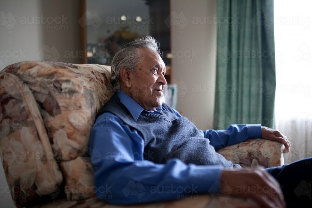 Elderly aboriginal man sitting in lounge chair at home - Australian Stock Image