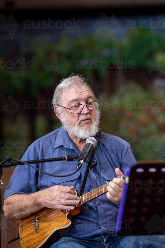 elderly gentleman playing ukulele and singing into microphone - Australian Stock Image