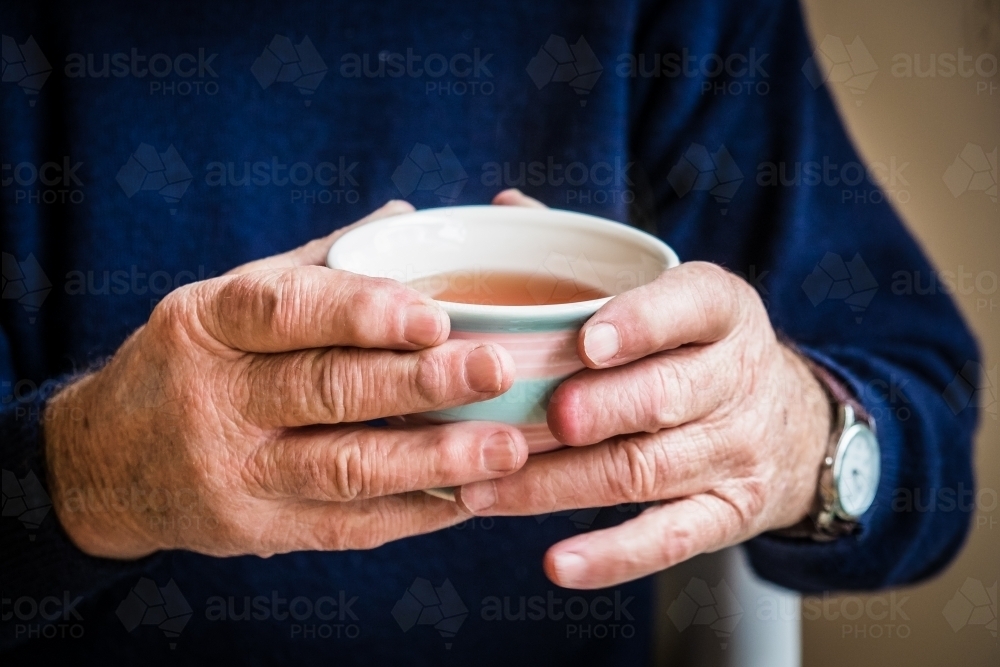 Elderly hands holding a warm cup of tea - Australian Stock Image