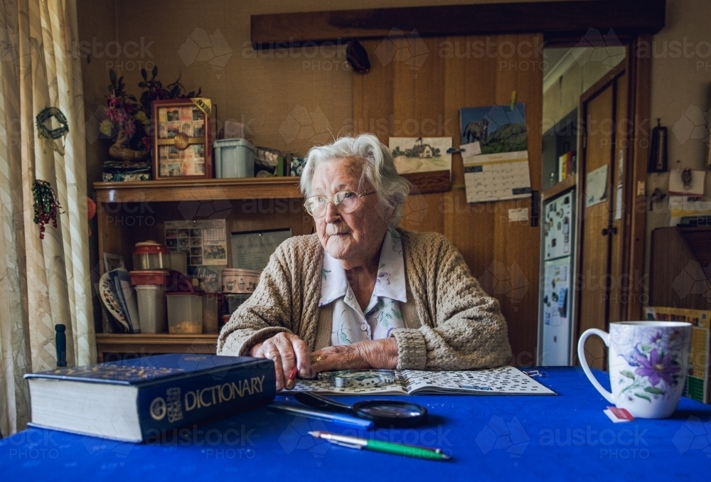 Elderly lady, a centenarian, at her dining table with the crossword puzzle and dictionary - Australian Stock Image