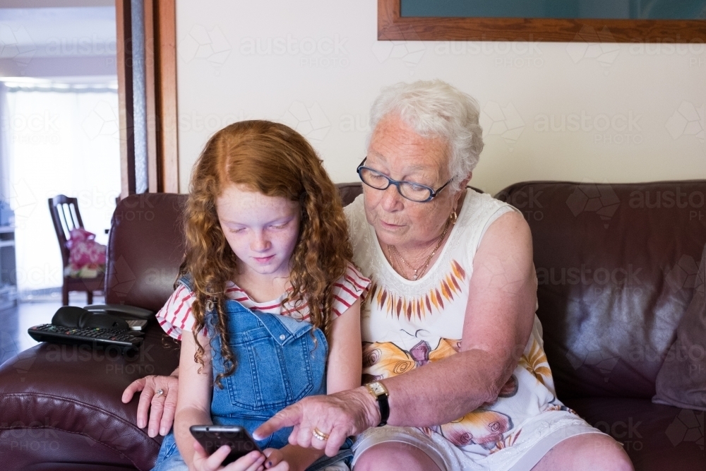 Elderly lady and young girl playing on a smartphone - Australian Stock Image