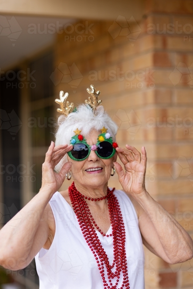 elderly lady dressed up in crazy christmas sunglasses outside her home - Australian Stock Image
