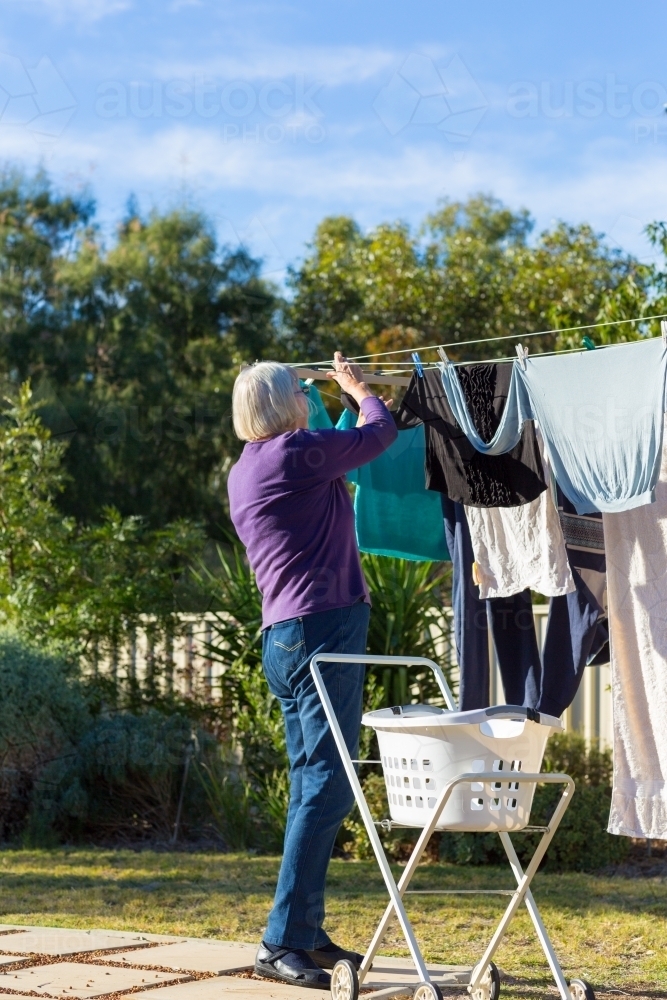 Elderly lady hanging clothes on washing line - Australian Stock Image