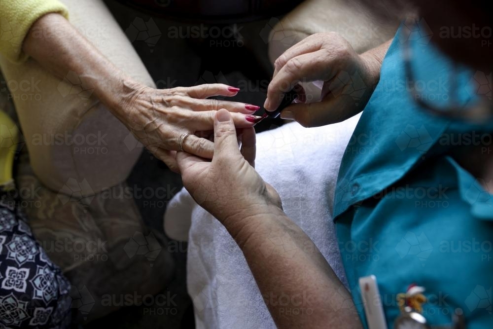 Elderly lady having nails painted by carer at nursing home - Australian Stock Image