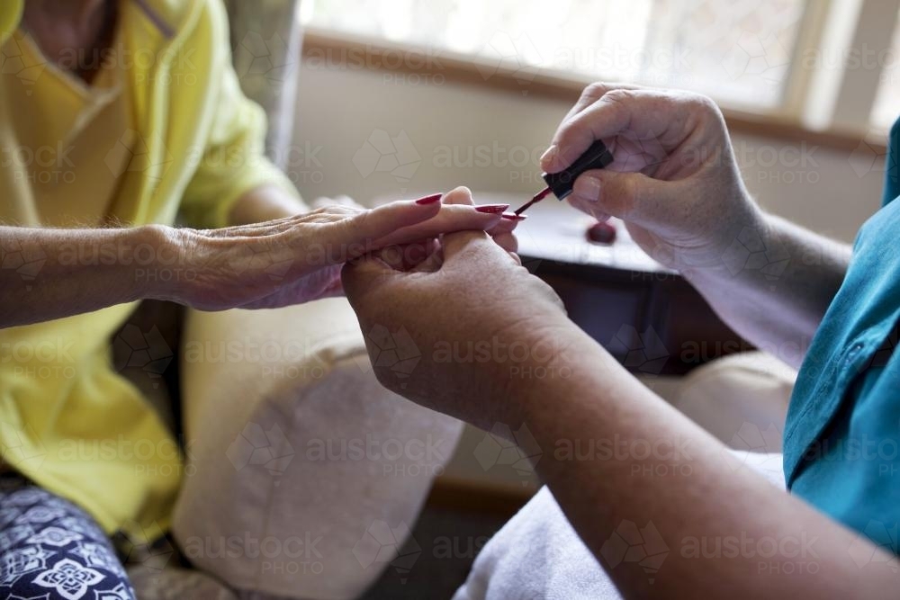 Elderly lady having nails painted by carer at nursing home - Australian Stock Image