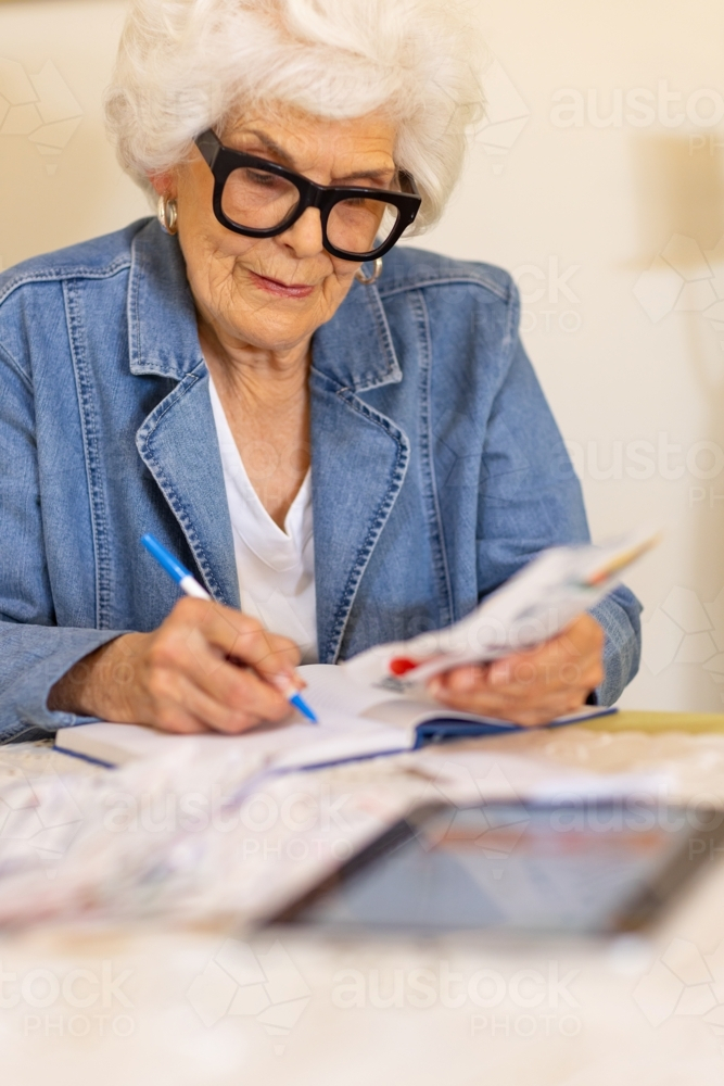 elderly lady sitting at table sorting out bills and receipts - Australian Stock Image